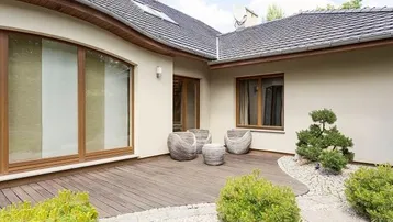 Moderne Holzterrasse mit stilvollen Sitzgelegenheiten und gepflegter Gartenbepflanzung am Haus.