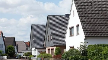 Reihenhäuser mit Satteldächern und gepflegten Vorgärten unter blauem Himmel in einer Wohnsiedlung.