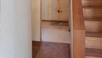 Flur mit Holztreppe und Zugang zu einem unfertigen Raum, der renoviert werden muss.
