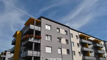 Modernes Mehrfamilienhaus mit grauer und beiger Fassade sowie gelben Akzenten und Balkonen.