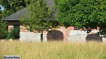 Altes Backsteingebäude mit Holztoren und dunklem Dach, umgeben von hohen Bäumen und Gras.