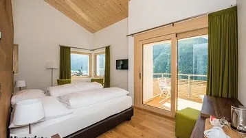 Helles Schlafzimmer mit Holzbalkendecke, Zugang zum Balkon und Bergblick, ausgestattet mit modernen Möbeln.