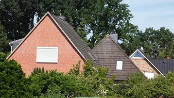 Mehrere Wohnhäuser mit Ziegeldächern und Backsteinfassaden, umgeben von üppigem Grün und Bäumen.