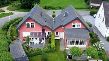 Luftaufnahme eines roten Doppelhauses mit gepflegtem Garten, Terrasse und grüner Umgebung.