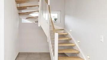 Helle Diele mit moderner Holztreppe, weißem Geländer und integrierter Wandbeleuchtung.