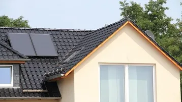 Dach eines modernen Hauses mit Photovoltaikanlage, Gaubenfenster und großem Giebelfenster.