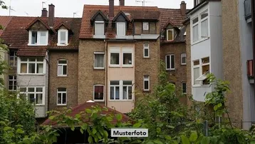 Mehrfamilienhaus mit Ziegelfassade, Dachgauben und einem Erker, umgeben von üppigem Grün.