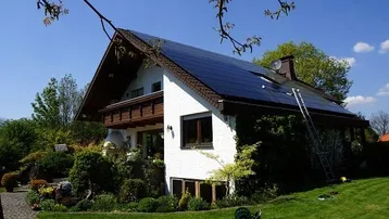 Freistehendes Haus mit Photovoltaikanlage auf dem Dach und gepflegtem Garten unter blauem Himmel.