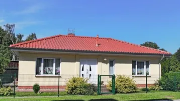 Einfamilienhaus mit rotem Ziegeldach, heller Fassade und gepflegtem Vorgarten unter blauem Himmel.