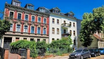 Historische Gebäude mit klassischer Architektur, gepflegter Fassade und Balkon an einem sonnigen Tag.