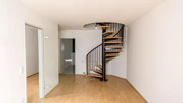 Heller, leerer Raum mit Holzfußboden und einer eleganten schwarzen Wendeltreppe, die in die obere Etage führt.