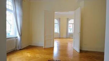 Helles Zimmer mit Fischgrätparkett, hohen Decken und großen Fenstern, typisch für einen Altbau.