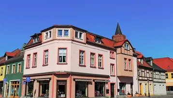 Historisches Eckgebäude mit Geschäften im Erdgeschoss und Wohnungen darüber, unter blauem Himmel.