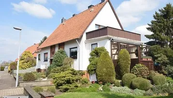Einfamilienhaus mit gepflegtem Vorgarten, Wintergartenanbau und einem kleinen Balkon im Obergeschoss.