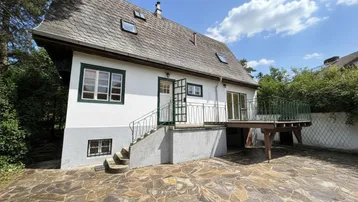 Charmantes Haus mit traditionellem Dach, Steinflächen und einer erhöhten Holzterrasse.