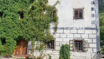 Altes Gebäude mit rustikaler Fassade, teilweise mit Efeu bewachsen und Holztüren.