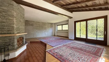 Geräumiges Wohnzimmer mit Kamin, Holzbalkendecke und großen Fenstern zum Garten.