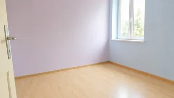 Helles, leeres Zimmer mit hellblauen und lila Wänden sowie einem Laminatboden.