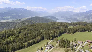 Panoramablick aus der Vogelperspektive auf das Anwesen mit umliegenden Wäldern, Bergen und einem See in der Ferne.