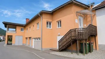 Gebäudeansicht mit orangefarbener Fassade, Außentreppe und Garagen unter blauem Himmel.
