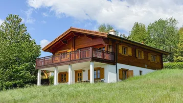 Traditionelles Holzhaus im Chalet-Stil auf einem grünen Hügel mit Balkon und Bergblick.