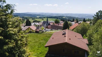 Panoramablick über ein malerisches Dorf mit Kirche und weiten grünen Hügeln unter blauem Himmel.