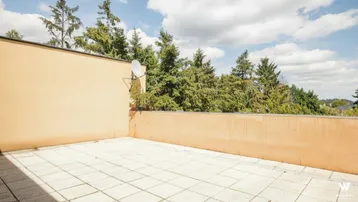 Geräumige, geflieste Terrasse mit hoher Brüstung und Blick ins Grüne, ideal für individuelle Gestaltung.