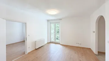 Helles Wohnzimmer mit Holzboden, Heizkörper und französischem Balkon, bereit zur individuellen Gestaltung.