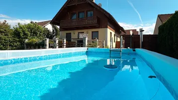 Außenpool mit klarem Wasser und Blick auf das charmante Einfamilienhaus.