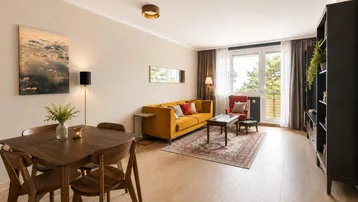 Helles Wohn- und Esszimmer mit modernem Mobiliar, Holzboden und Zugang zu einem Balkon mit grüner Aussicht.