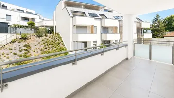 Geräumiger, unmöblierter Balkon mit Fliesenboden und Blick auf die moderne Wohnanlage.