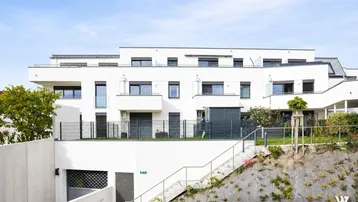Moderne Wohnanlage mit weißer Fassade, Terrassen und Zugang zur Tiefgarage.