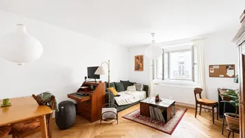 Helles Wohnzimmer mit Fischgrätparkett, einem Esstisch und einem Arbeitsbereich am Fenster.