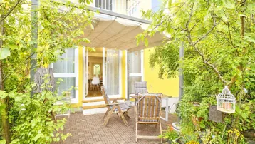 Gemütliche Terrasse mit Gartenmöbeln und Sonnenschutz, umgeben von üppigem Grün.