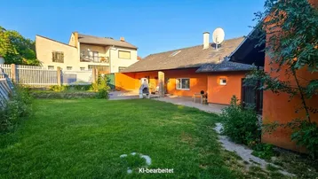 Gartenbereich mit Rasenfläche, Terrasse und Grillplatz hinter dem orangefarbenen Haus.