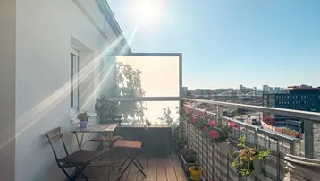 Sonnige Dachterrasse mit Holzboden, Sitzgelegenheiten und weitem Blick über die Stadt.