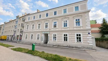 Klassisches Mehrfamilienhaus mit eleganter, heller Fassade und verzierten Fenstern an einer städtischen Straße.