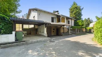 Einfamilienhaus mit Carport und Zufahrt in grüner Umgebung.