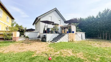 Hinteransicht des Hauses mit großer Terrasse, Treppe zum Garten und Rasenfläche.