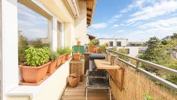 Schmaler Balkon mit Holzboden, Pflanzen und einem kleinen Tisch, ideal für entspannte Stunden im Freien.