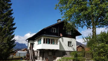 Traditionelles Haus mit Bergblick und großem Gartenbereich unter blauem Himmel.
