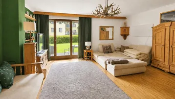 Gemütliches Wohnzimmer im alpinen Stil mit Holzboden, grüner Akzentwand und Zugang zum Garten.