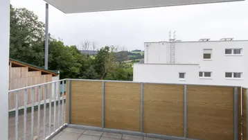 Heller Balkon mit Fliesenboden, Holzsichtschutz und Blick ins Grüne.