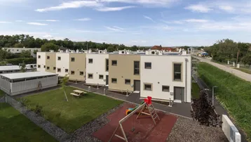 Moderne Reihenhäuser mit Flachdach, umgeben von Grünflächen und einem Kinderspielplatz.
