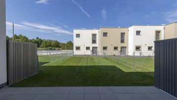 Gepflasterte Terrasse mit Rasenfläche und Blick auf die modernen Reihenhäuser.