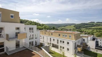 Moderne Wohnanlage mit weißer Fassade, Balkonen und weitem Blick ins Grüne.
