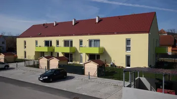 Moderne Wohnanlage mit gelber Fassade, roten Dächern und Balkonen mit grünen Brüstungen.