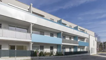 Moderne Wohnhausfassade mit blauen Akzenten und Balkonen unter blauem Himmel.