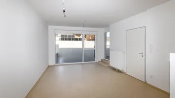 Helles, leeres Wohnzimmer mit Zugang zu einem Balkon und großen Fenstern.