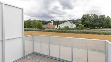 Balkon mit Fliesenboden und weitem Blick über Felder und eine Kirche.
